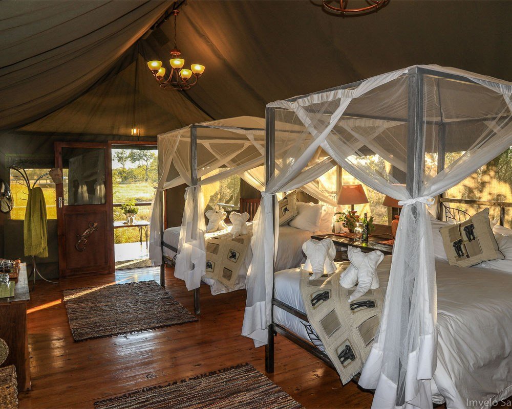 A tent at Bomani Tented Lodge has two canopy beds, wooden floors and a chandelier