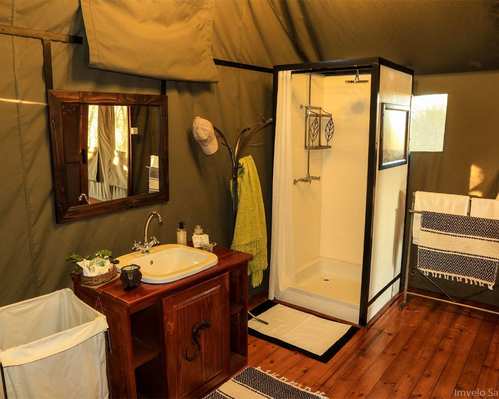 A tent bathroom at Bomani Tented Lodge has a glass shower and wooden vanity