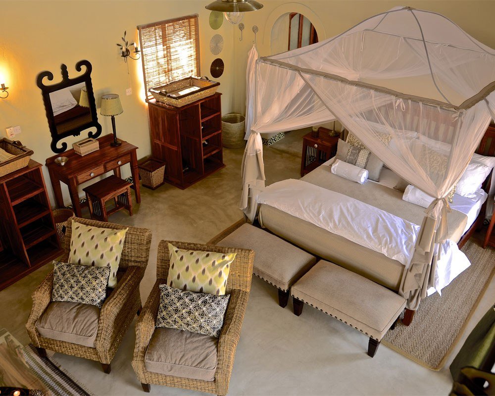 A villa bedroom at Camelthorn Lodge has a canopy bed and woven armchairs