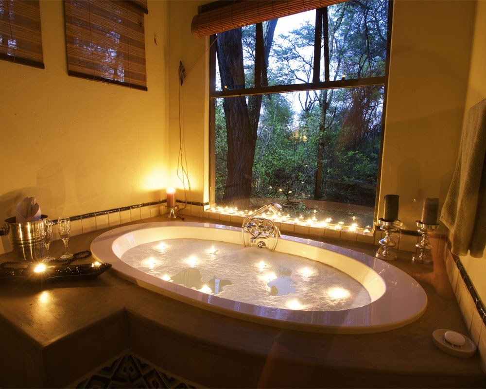 A sunken bath at Camelthorn Lodge is lit with candles beside a window onto the trees