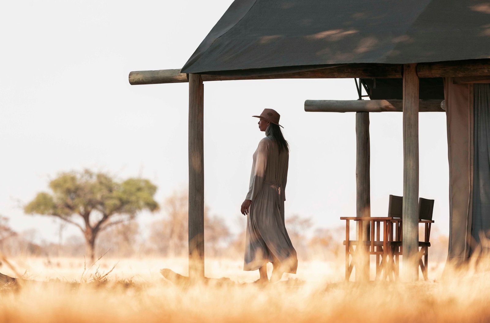 A guest on a tent's deck at Wilderness Davison's Camp looks over dry grassland in Hwange