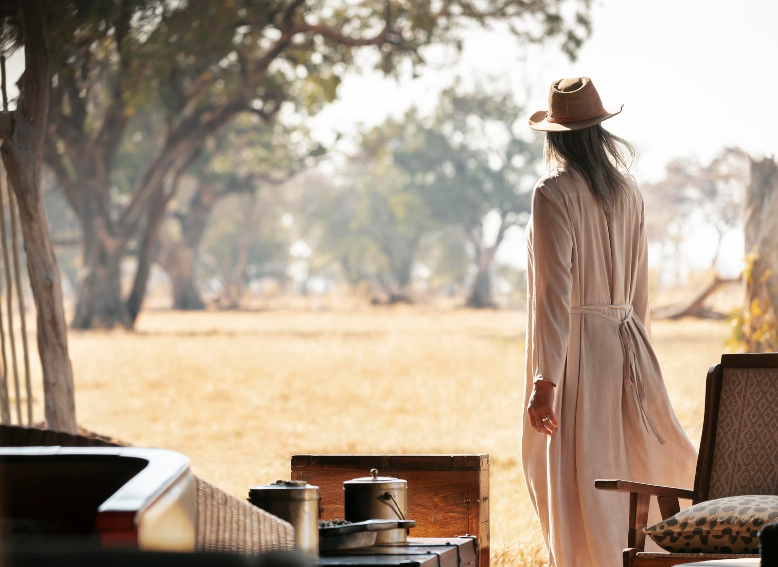 A guest in a hat steps from the tent at Wilderness Davison's Camp towards open woodland