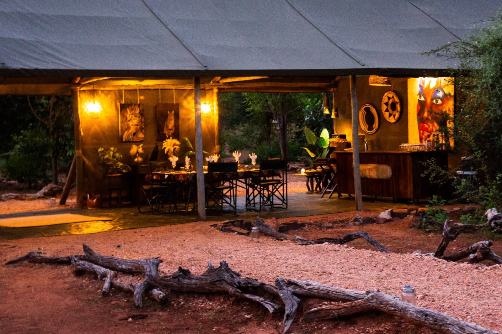 Hwange Bush Camp's main dining and lounge area lights up at night, with deadwood in front