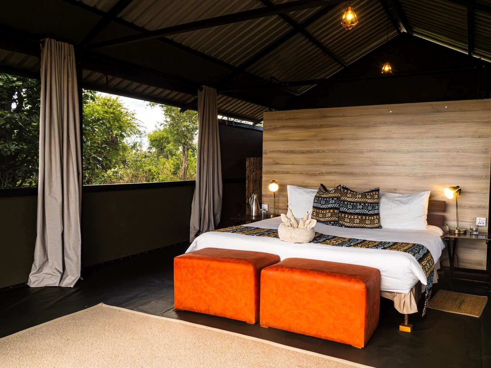 A room at Hwange Bush Camp has a double bed, orange ottomans and open sides
