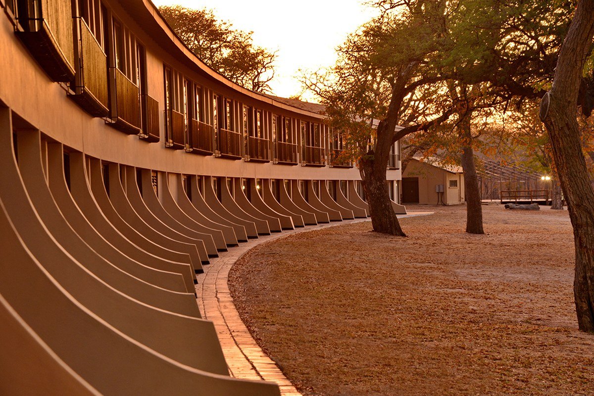 Hwange Safari Lodge's long curved wing of rooms faces open ground at sunset