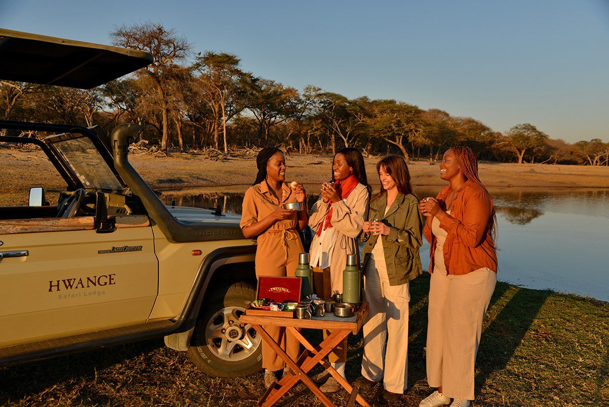 Guests from Hwange Safari Lodge enjoy sundowners beside a game vehicle at the water's edge