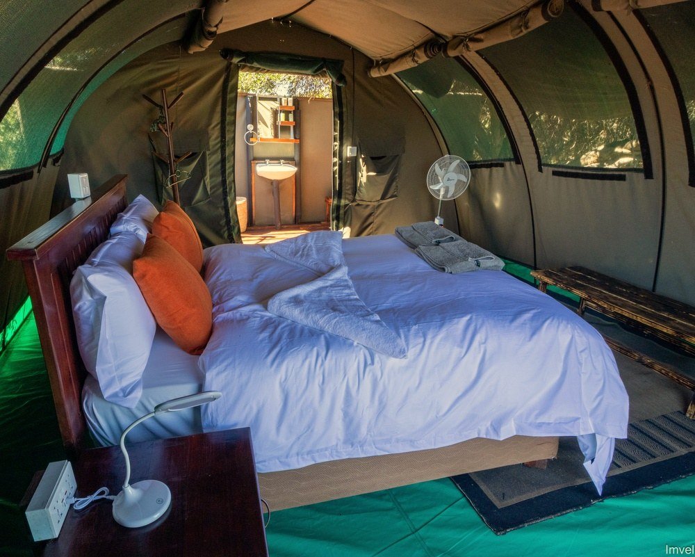 A tent bedroom at Jozibanini Camp has white linen and orange cushions