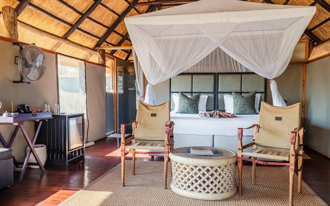 A bedroom at Khulu Bush Camp has a canopy bed and safari chairs on the floor