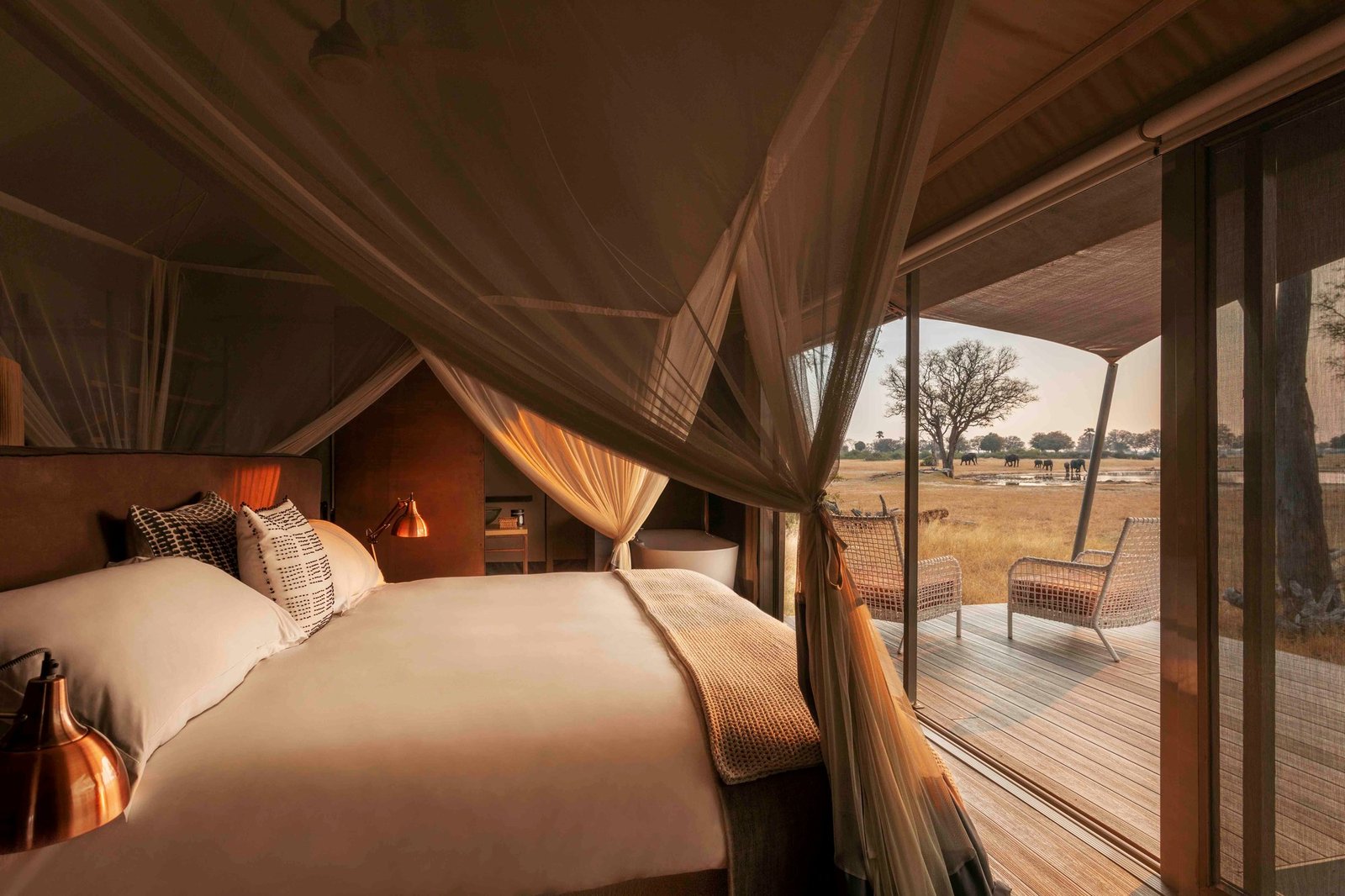 Inside a tented suite at Wilderness Linkwasha, a canopy bed faces glass doors to the deck