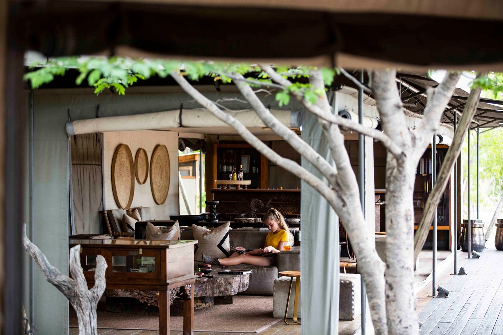 The open-sided lounge at Wilderness Little Makalolo wraps around a tree trunk, with a guest reading