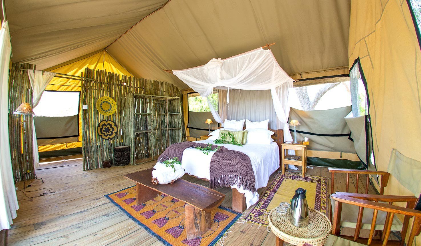A tent at Miombo Safari Camp has a canopy bed, rugs and wooden furniture