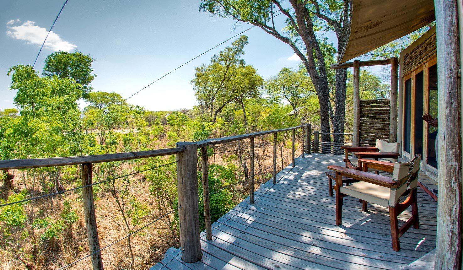 A tent's wooden deck at Miombo Safari Camp has chairs looking over green bush