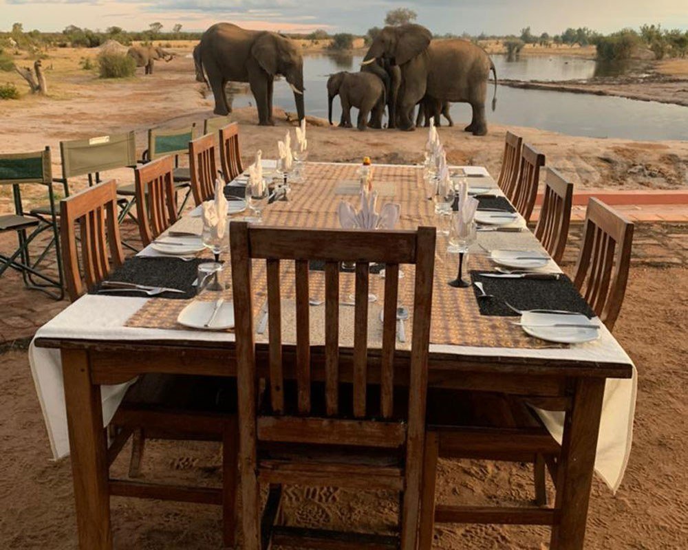 At Nehimba Lodge, the dining table is laid on the deck as elephants drink beyond