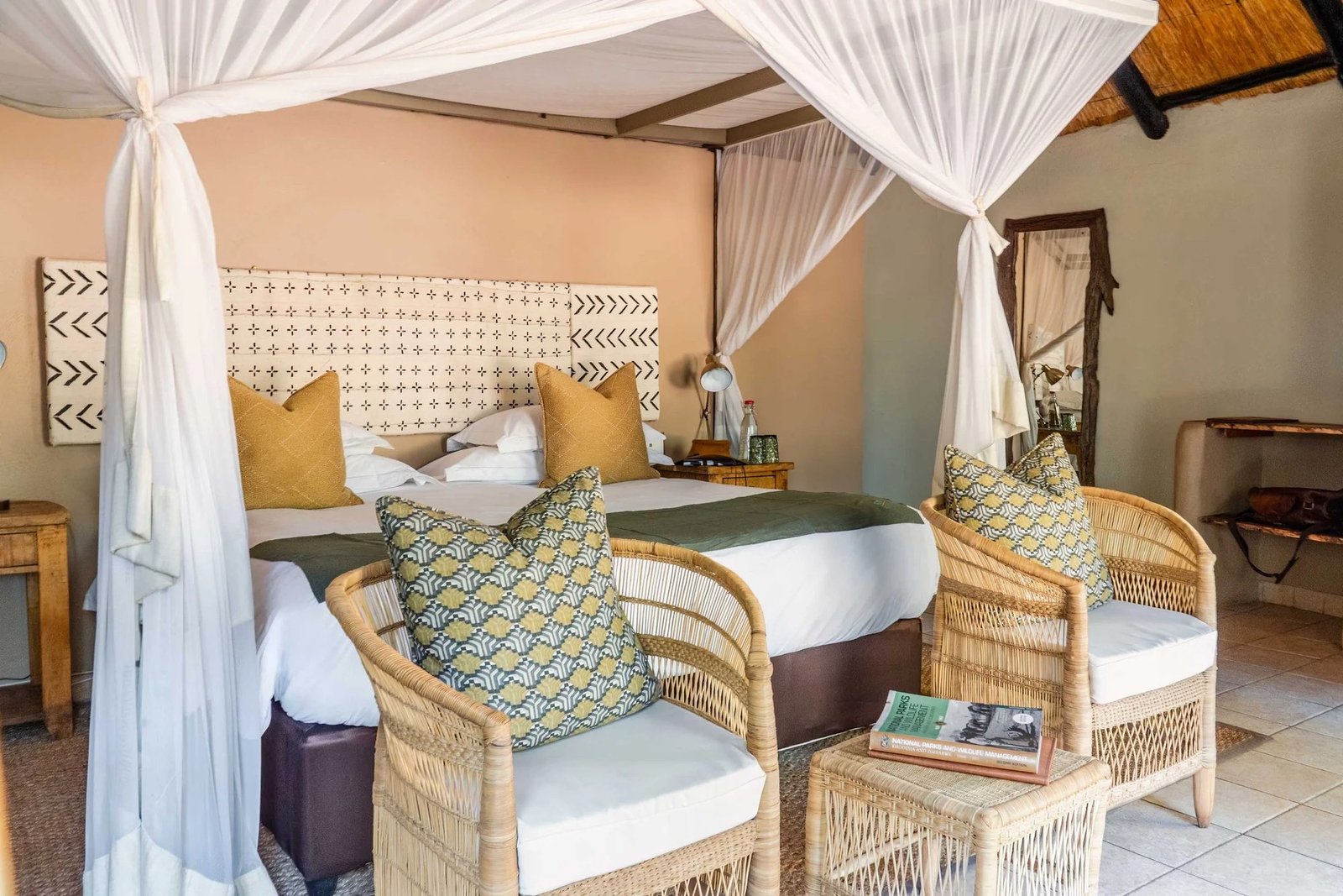 A bedroom at Sable Valley Lodge has a canopy bed, cushions and woven armchairs