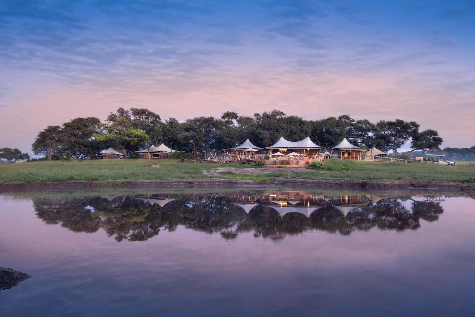 Somalisa Camp's tents sit beneath a stand of trees, reflected in the Hwange pan at dusk