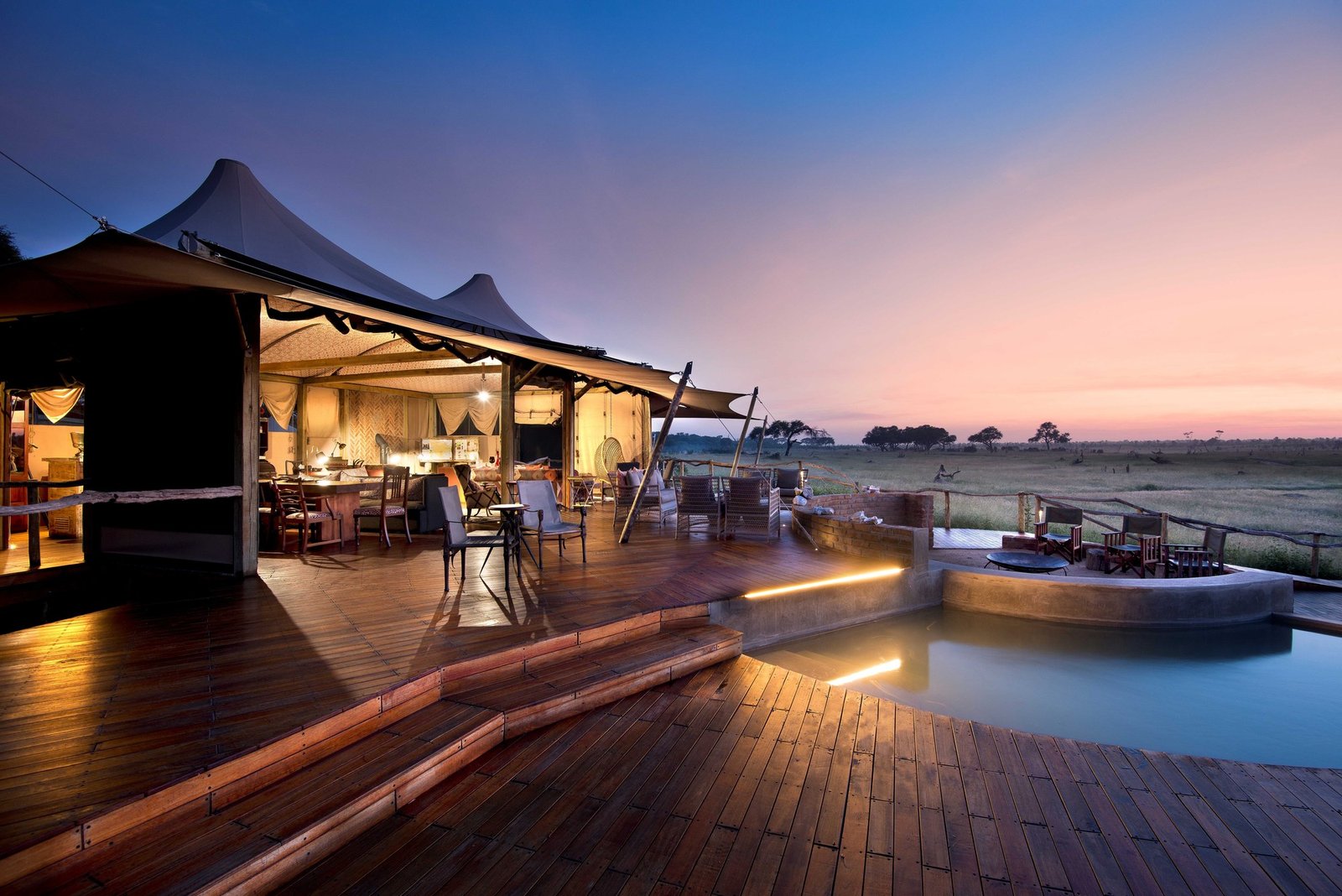 At dusk, Somalisa Camp's main deck glows, with the lounge, fire pit and pool lit