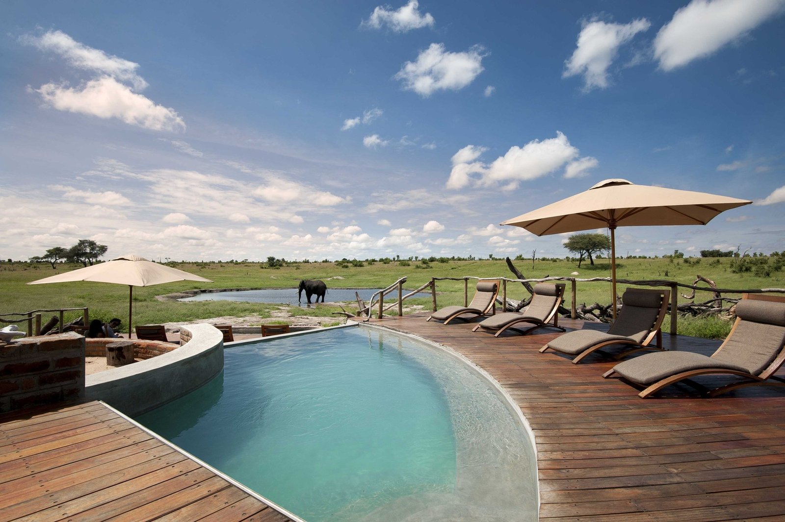 The pool and loungers at Somalisa Camp face the open pan, with an elephant beyond