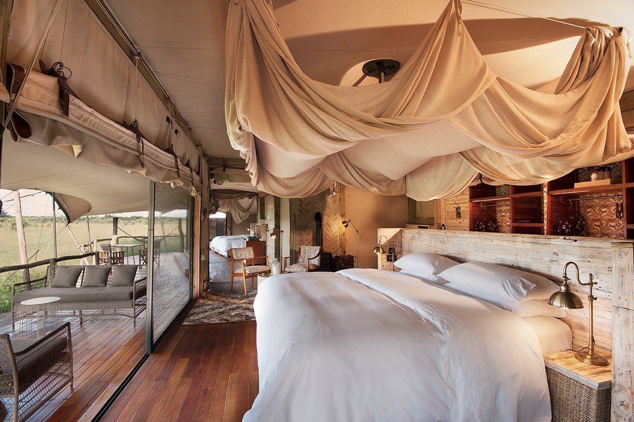 A bedroom at Somalisa Camp has a large white bed, wooden floors and open sides