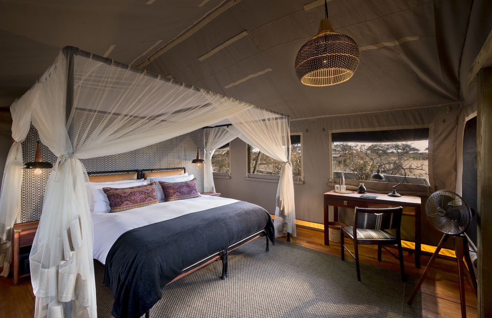 A tented room at Somalisa Expeditions has a canopy bed and dark wooden furniture