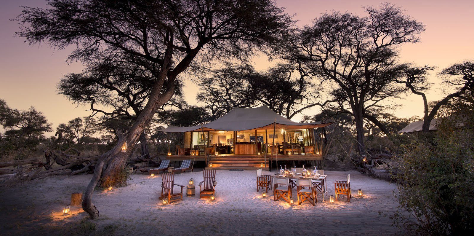 Somalisa Expeditions' main area lights up at dusk, with tables set beneath the trees