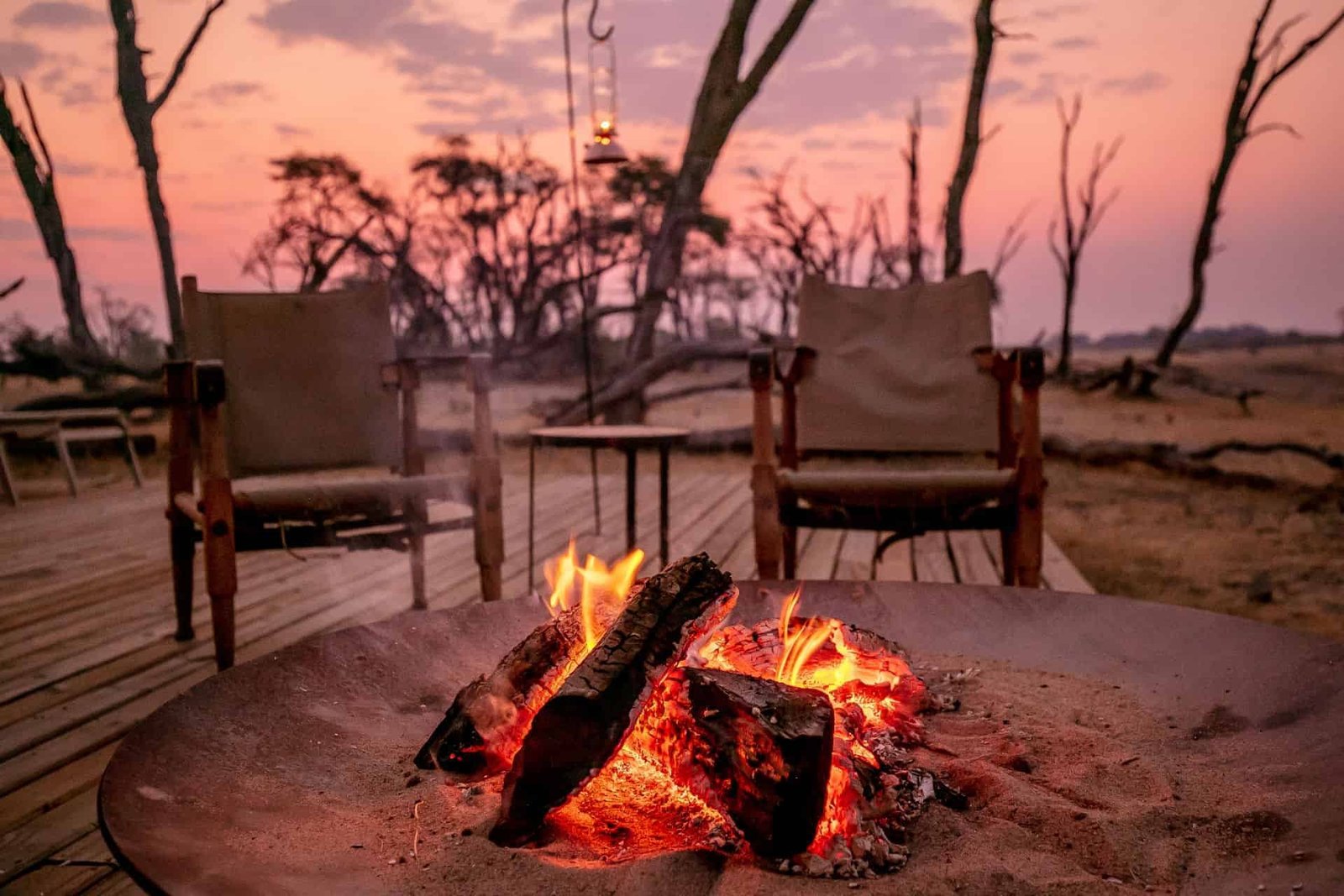 Chairs circle the fire pit on the deck at The Hide Safari Camp at dusk