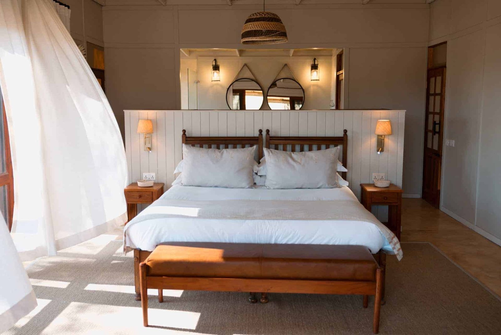 A bright bedroom at The Hide Safari Camp has a double bed and white curtains