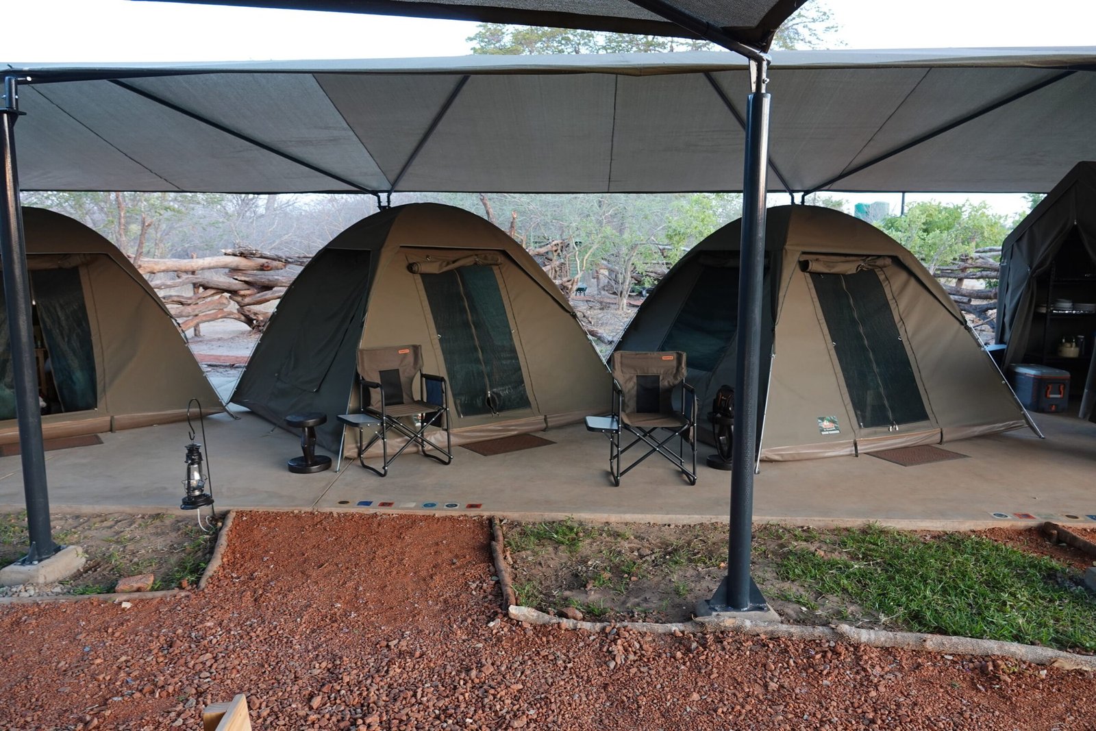 Dome tents at The Siding in Hwange stand under shade canopies along a red gravel path